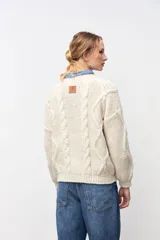 Cardigan de punto grueso color crudo, con diseño de trenzas verticales, cuello redondo y cierre frontal con botones oscuros.