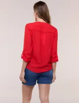 Blusa de calce relajado color salmón, confeccionada en tela liviana con textura sutil. Presenta escote en V con abotonadura frontal, bolsillo parche en el pecho, mangas largas regulables con presilla y ruedo con opción de anudar en el frente.