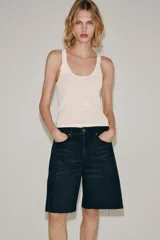 Bermuda de denim color marrón oscuro, de tiro medio y diseño relaxed fit, con cinco bolsillos, trabillas para cinto, bajo desflecado y cierre frontal con cremallera y botón.