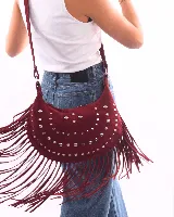 Bolso de hombro estilo boho confeccionado en gamuza color bordó. Presenta un diseño semicircular decorado con tachas metálicas plateadas dispuestas en líneas curvas y flecos largos en todo el borde inferior. Cuenta con cierre superior y correa ajustable para llevar al hombro.