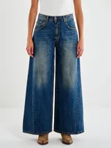 Jeans de mezclilla azul oscuro con lavado vintage y efecto degradado en las piernas. Diseño de tiro medio con pierna muy ancha (palazzo o culotte ancho) y costura central vertical en el frente de cada pierna.