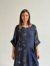 Vestido largo azul oscuro con diseño asimétrico que combina un lado liso con un lado estampado de hojas, manga corta y bolsillo frontal aplicado.