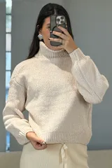 Buzo de chenille color blanco, con cuello alto tipo polera, mangas largas con puños ajustados y diseño de tejido acanalado.