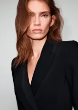 Vestido tipo blazer de corte corto y color negro, con solapas de muesca, doble botonadura frontal y bolsillos de ojal con solapa.