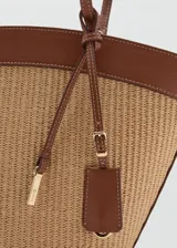 Bolso shopper grande estilo capazo, confeccionado en tejido texturizado efecto rafia en tono beige, combinado con detalles de cuero sintético marrón en los bordes y las asas dobles de hombro. Cuenta con cierre de cremallera superior y un charm colgante decorativo.