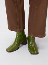 Botas de caña media color marrón, confeccionadas en cuero con acabado brillante. Presentan punta cuadrada, taco de madera y un distintivo bordado decorativo en color rojo que recorre el empeine hasta la punta.