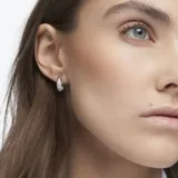 Par de aros tipo argolla Swarovski Dextera, con cristales blancos engarzados en pavé y baño de rodio. Diseño escultural moderno.