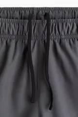 Short deportivo gris con calza interior negra, corte estándar, con cintura elástica y cordón ajustable.