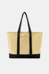 Bolso shopper de lona color beige con base, asas y tiras frontales en color negro. Cuenta con un bolsillo frontal con botón a presión y costuras visibles en contraste.