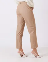 Pantalon de corte cigarette en color beige, confeccionado en tejido con apariencia denim y acabado satinado. Presenta tiro medio-alto, largo tobillero, cintura con presillas, cierre con gancho sastrero oculto, bolsillos laterales diagonales con botones forrados y pinzas traseras para un ajuste entallado.