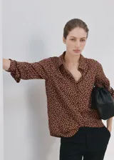 Camisa de poliéster color marrón con estampado de lunares blancos, cuello camisero, manga larga y cierre frontal de botones ocultos.