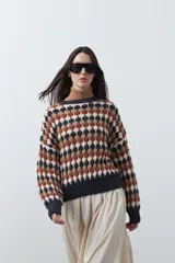 Sweater de punto con diseño geométrico de rombos en tonos azul, marrón, beige y blanco. Presenta cuello redondo, puños y ruedo acanalados en color azul oscuro, con un calce relajado y mangas largas.
