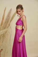Vestido largo de satén color fucsia, con escote en V, aberturas laterales en la cintura y detalle de aro metálico en el centro del pecho. Posee breteles finos y falda con caída fluida.