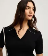 Blusa negra de punto con cuello polo, escote en V y mangas cortas. Detalle de mini perlas aplicadas en el cuello.