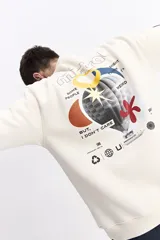 Buzo de algodón color crema, corte oversize, con escote redondo y puños. Presenta un estampado gráfico grande en la espalda con un globo aerostático y texto que incluye "SOME PEOPLE MIGHT THINK I'M WEIRD BUT, I DON'T CARE" y otros símbolos gráficos.