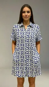 Vestido camisero de corte holgado y silueta relajada, con cuello clásico, cierre frontal de botones y mangas cortas con dobladillo. Presenta un estampado de cuadros irregulares en color bordó sobre fondo blanco.