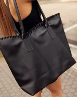 Bolso tipo tote de cuero negro, hecho a mano, con detalle de costura decorativa en el borde superior y asas largas para llevar al hombro.