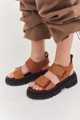 Sandalias marrones con tiras de cuero con ajuste de velcro y detalles en amarillo.