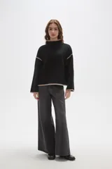 Polera de tejido de punto color negro con detalles de vivos en color beige en el cuello, puños, ruedo y costuras de las mangas. Presenta un diseño holgado con cuello alto y mangas largas.