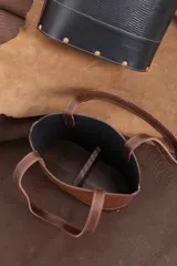 Cartera matera de cuero vacuno negro con textura símil lagarto, diseño estructurado con base ovalada y doble asa de hombro. Cuenta con detalles de tachas metálicas doradas y costuras pespunteadas en contraste.