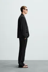 Blazer negra relaxed fit confeccionada en tejido fluido con mezcla de lyocell. Cuello con solapas de muesca y manga larga. Bolsillos de solapa en cadera. Detalle de bolsillo interior. Cierre frontal de botonadura.