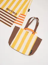Bolso tipo tote con diseño de rayas verticales en amarillo y blanco, con laterales, base y correas en color marrón. Incluye asas cortas en color naranja y cierre con botón a presión.