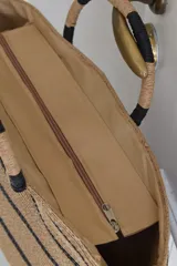 Bolso tipo tote confeccionado en material tejido color tostado con diseño de rayas horizontales negras y asas de mano circulares rígidas envueltas.