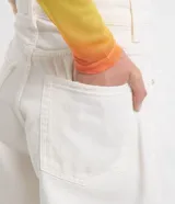 Short de sarga color blanco, corte mom, tiro alto, con trabillas en la cintura y bolsillos. Tiene cierre tradicional por botón y cremallera.