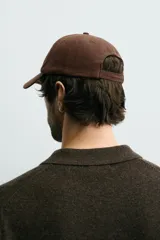 Gorra de seis paneles confeccionada en tejido de algodón, color marrón, con bordado frontal en color crema que incluye texto. Cuenta con ajuste en la parte posterior.