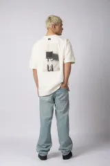 Remera oversize de algodón 100% premium, color blanco hueso, con bordado frontal "90's" en negro y un parche trasero con una imagen estilo videoclip de Nirvana.