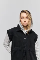 Chaleco de jean negro, de calce relajado con hombros caídos, cuello camisero, cierre frontal con botones y grandes bolsillos aplicados.