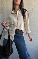 Camisa beige de manga larga con detalles bordados en la botonera y el cuello, cierre frontal con botones y diseño fluido.