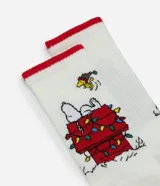Par de medias blancas de caña larga con puños, talón y puntera en color rojo. Presentan un estampado navideño de Snoopy sobre su casita decorada con luces de colores.