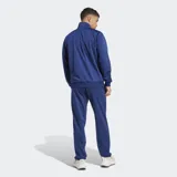 Conjunto deportivo Adidas de dos piezas, campera y pantalón, en color azul. Campera de cuello alto con cierre frontal completo y bolsillos laterales, y pantalón con cintura elástica con cordón ajustable y bolsillos laterales.