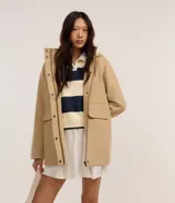 Campera alargada de polivelour color beige, con capucha, cierre frontal con cremallera y solapa con botones a presión, bolsillos con solapa y mangas largas.
