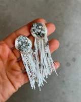 Caravanas colgantes con base circular decorada con cristales y piedras, y flecos largos de hilo blanco combinados con cadenas de strass.