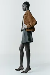 Falda pantalón de tiro alto con diseño de tablas, confeccionada en tejido gris. Incluye un cinturón fino de cuero sintético con hebilla metálica dorada y cierre lateral con cremallera oculta.