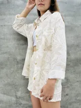 Conjunto de camisa y short beige con estampado de hojas, camisa de manga larga con botones y short con bolsillos laterales.