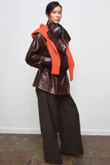 Chaqueta amplia de efecto piel en color marrón oscuro, con cuello alto, manga larga y bolsillos delanteros. Presenta cintura ajustable, forro interior y cierre frontal con cremallera y botones ocultos por solapa.
