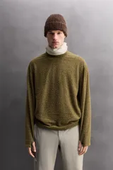 Sudadera de ajuste regular, color verde oliva, con cuello redondo y manga larga. Presenta una textura irregular en el tejido, similar al borreguito o bouclé.