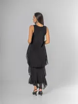 Vestido largo negro de seda con escote en V adornado con lentejuelas plateadas. Presenta un diseño de capas superpuestas con terminaciones deshilachadas que aportan volumen y movimiento. Es de corte sin mangas con breteles anchos y espalda elastizada.