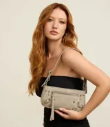 Cartera tipo baguette de PU color beige claro, con acabado liso y detalles de apliques metálicos tipo tachas y argollas en color gunmetal. Presenta un bolsillo frontal con cierre y un tirador de cuero sintético colgante. Incluye asa corta ajustable con hebilla.