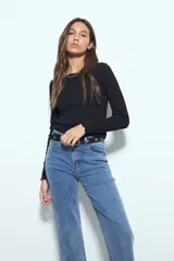 Remera de manga larga con ajuste al cuerpo, confeccionada en tejido acanalado de color marrón. Presenta cuello redondo y terminaciones con borde ondulado en puños y ruedo.