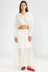 Camisa cropped de manga larga confeccionada en crepé color crema, con cuello camisero, botones frontales y elástico en la cintura.