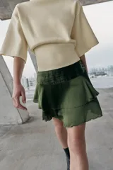 Falda corta de satén color verde oliva, con cintura fruncida y dos niveles de volantes con terminación ondulada.