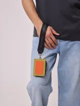 Tarjetero Rusty Runoi con cierre y correa para colgar, confeccionado en poliuretano color verde con aplique naranja y logo de la marca.