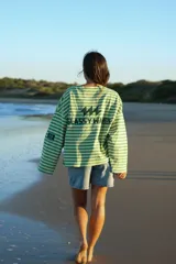 Buzo reversible de manga larga, con un lado a rayas horizontales verdes y blancas, y el otro lado liso verde. Presenta un estampado en la espalda con el texto "GLASSY WAVES" y un logo de rayos.