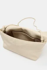 Bolso de mano tipo sobre en color beige, con diseño acolchado y solapa frontal. Cuenta con cierre imantado, bolsillo interior y correa bandolera extraíble.
