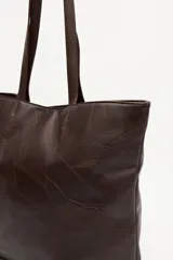 Cartera tote negra de símil cuero con diseño texturizado de parches y asas largas.