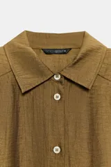 Camisa de corte recto confeccionada en tejido con mezcla de lino, color marrón. Presenta cuello solapa, cierre frontal con botones, mangas largas con puños y hombreras marcadas que aportan estructura.